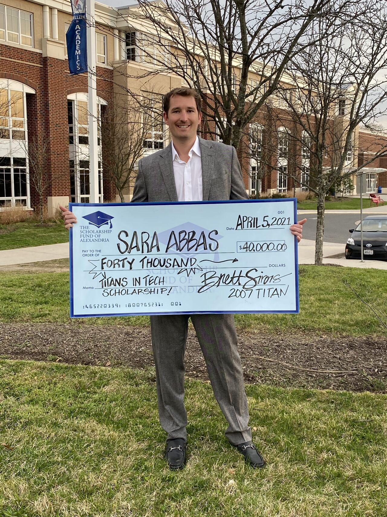 A man outside a school holding a ceremonial $40,000 Titans in Tech scholarship check made out to Sara Abbas, dated April 5, 2021.